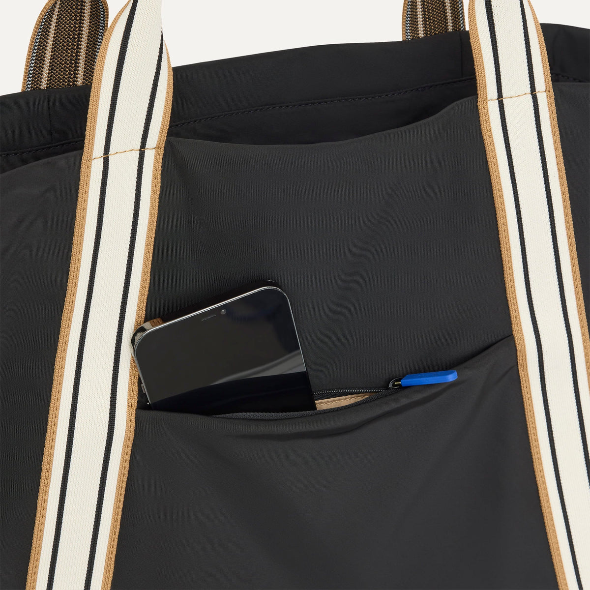A close up of The Travel Tote in Ink with a phone slipped into the outer pocket.
