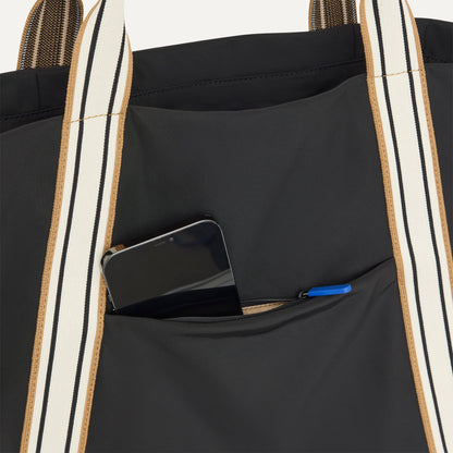 A close up of The Travel Tote in Ink with a phone slipped into the outer pocket.