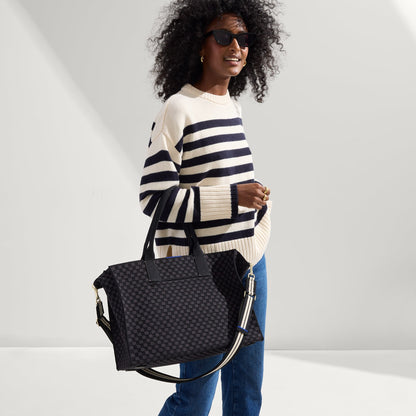 Overlay:: Shown with The Crossbody Strap (sold separately.) | Alt:: The Classic Tote in Black Sand, carried by its top handles by a model, shown from side.